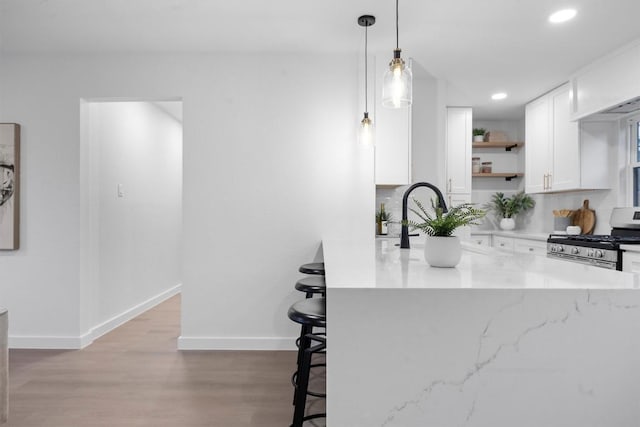 kitchen featuring stainless steel gas stove, light wood finished floors, a kitchen bar, white cabinetry, and open shelves