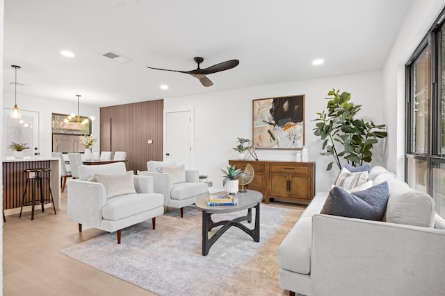 living area with ceiling fan with notable chandelier, light wood-type flooring, visible vents, and recessed lighting