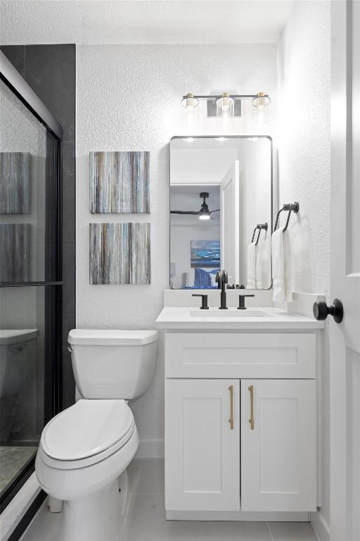 bathroom with a stall shower, a ceiling fan, a textured wall, toilet, and vanity