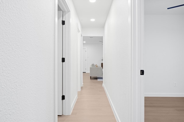 hallway with a textured wall, recessed lighting, light wood-type flooring, and baseboards