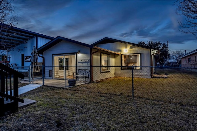 back of house at dusk with a gate, fence, and a lawn