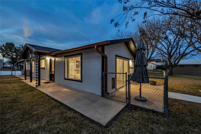 view of side of property with a gate, fence, a lawn, and stucco siding