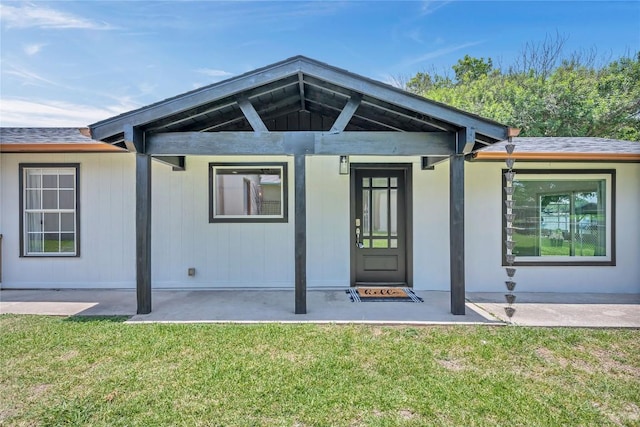 entrance to property with a yard, roof with shingles, and a patio