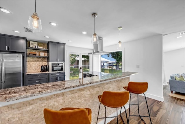 kitchen with light stone countertops, decorative light fixtures, island exhaust hood, and stainless steel refrigerator