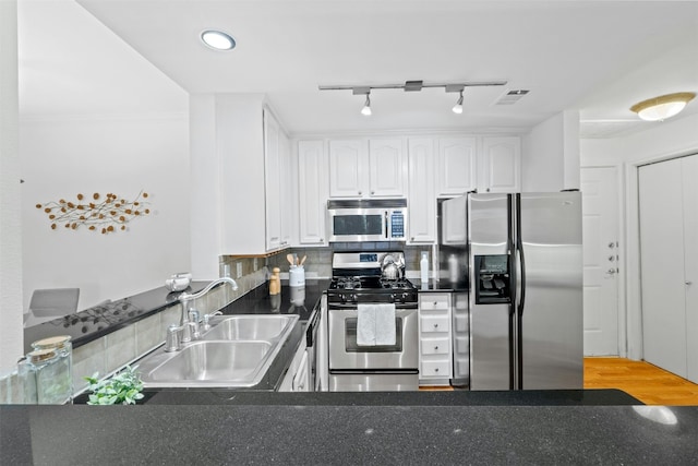 kitchen with decorative backsplash, white cabinets, dark countertops, appliances with stainless steel finishes, and a sink