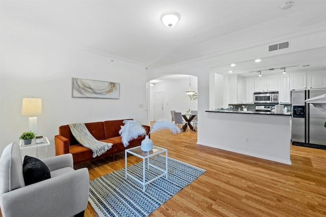 living area with arched walkways, visible vents, light wood-style floors, ornamental molding, and track lighting