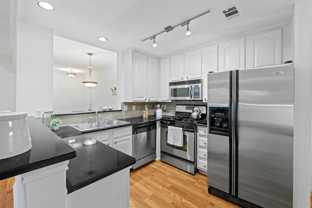 kitchen featuring dark countertops, visible vents, appliances with stainless steel finishes, a sink, and a peninsula