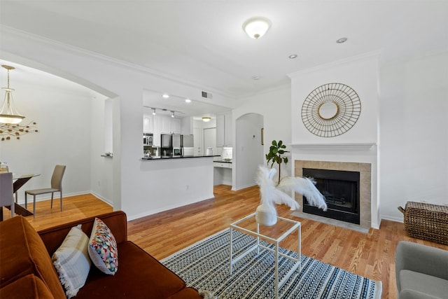 living room with arched walkways, a fireplace, baseboards, ornamental molding, and light wood finished floors