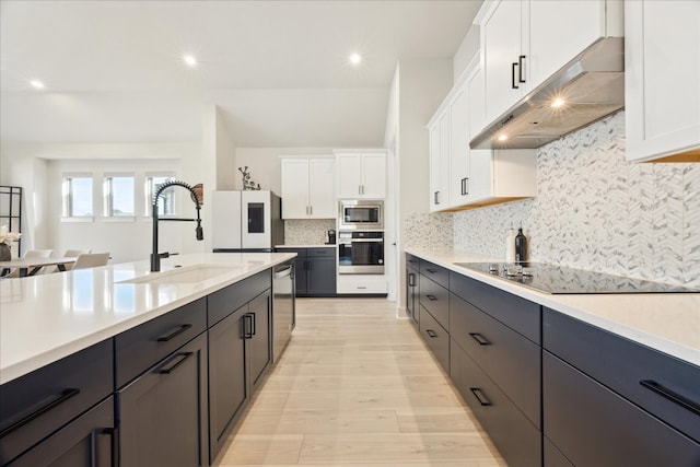 kitchen with light countertops, appliances with stainless steel finishes, white cabinets, a sink, and under cabinet range hood