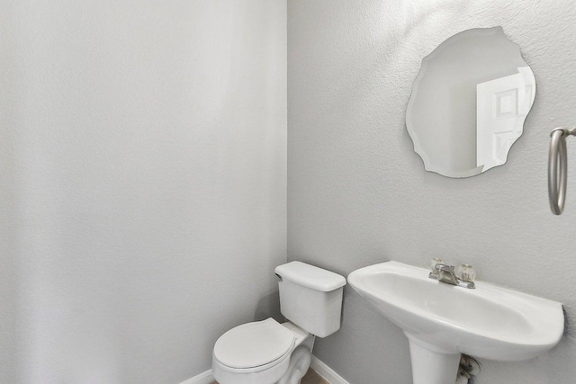 half bath featuring a sink, toilet, and baseboards