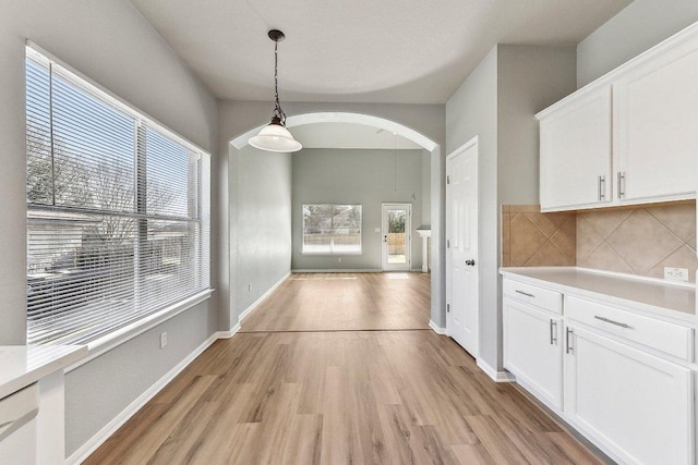 unfurnished dining area featuring light wood-type flooring, arched walkways, and baseboards
