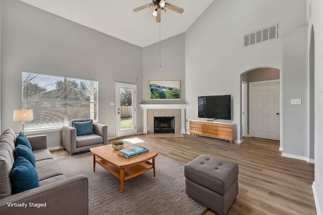 living area with arched walkways, visible vents, light wood finished floors, and a tiled fireplace