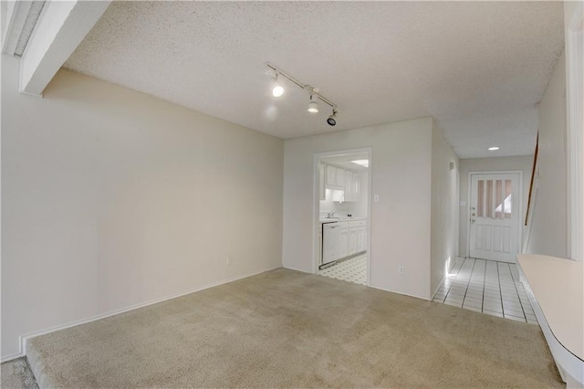 spare room featuring rail lighting, light carpet, a textured ceiling, and light tile patterned floors