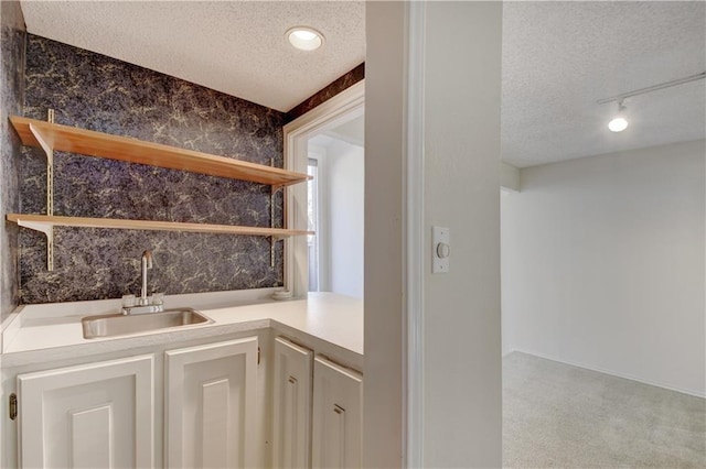 bar with a sink, a textured ceiling, track lighting, and wallpapered walls