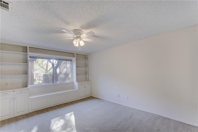 empty room featuring a ceiling fan, light colored carpet, visible vents, and a textured ceiling