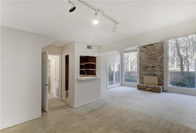 carpeted empty room with a textured ceiling, rail lighting, and visible vents