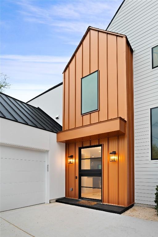 view of front facade featuring concrete driveway, metal roof, an attached garage, a standing seam roof, and board and batten siding