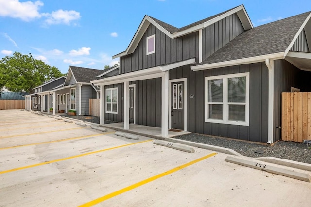 exterior space with roof with shingles, uncovered parking, board and batten siding, a porch, and fence