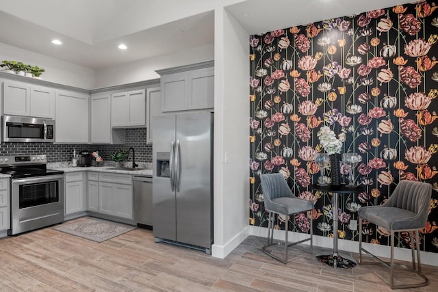 kitchen with recessed lighting, light wood-style flooring, backsplash, stainless steel appliances, and a sink
