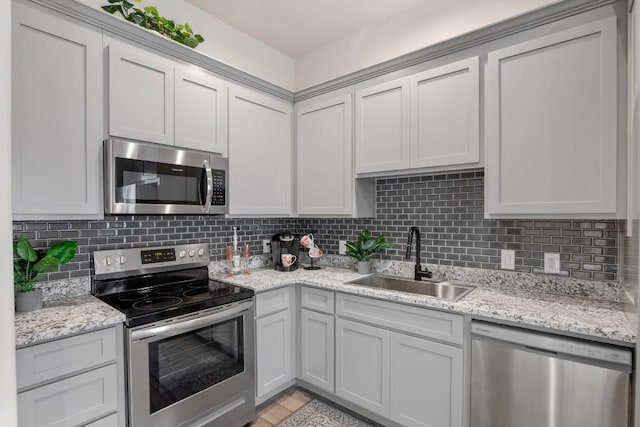 kitchen with appliances with stainless steel finishes, a sink, light stone counters, and decorative backsplash