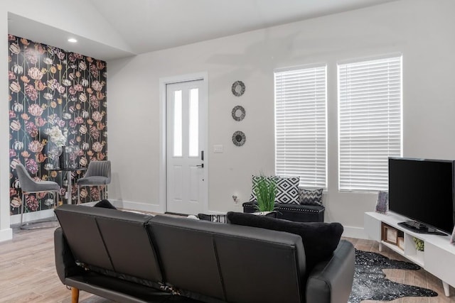 living area featuring baseboards, light wood-style floors, and vaulted ceiling