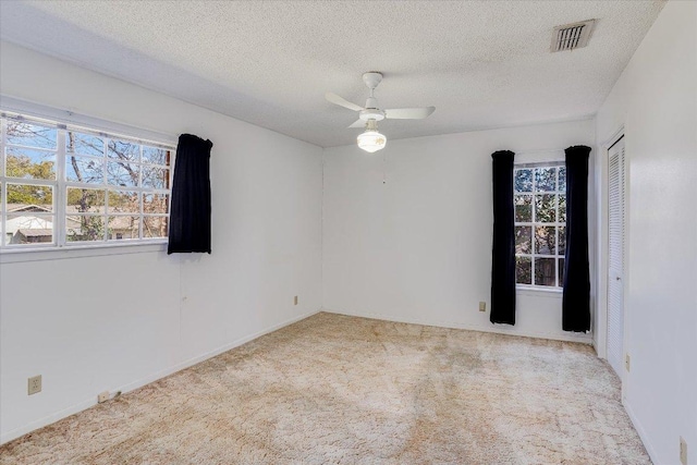 carpeted empty room with ceiling fan, visible vents, and a textured ceiling