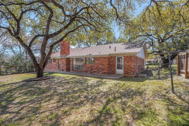 back of house featuring a yard, brick siding, fence, and a chimney