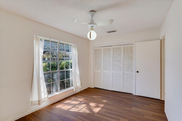 unfurnished bedroom with a closet, visible vents, a textured ceiling, and wood finished floors