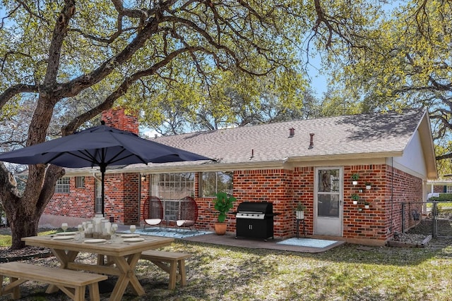 back of house with a patio, brick siding, a yard, roof with shingles, and a chimney