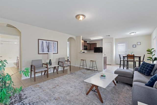 living area with arched walkways, visible vents, baseboards, and light tile patterned floors