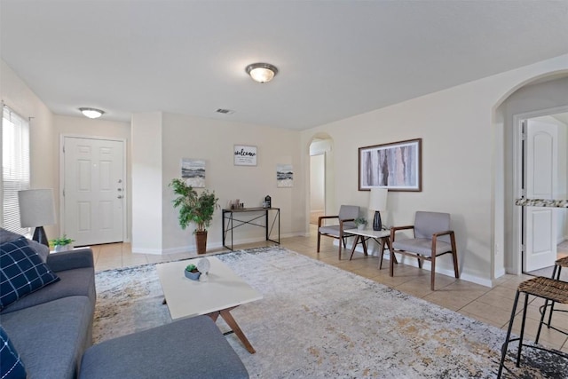 living area featuring arched walkways, light tile patterned flooring, visible vents, and baseboards