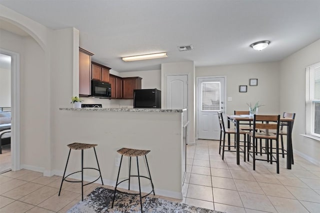 kitchen featuring light tile patterned floors, a kitchen breakfast bar, a peninsula, fridge, and black microwave