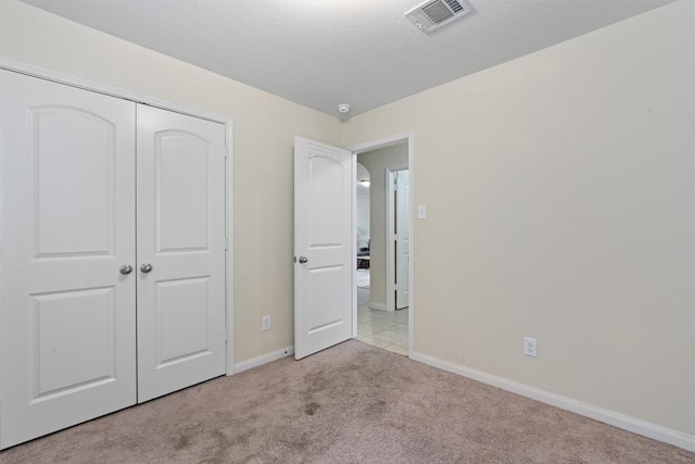 unfurnished bedroom with a textured ceiling, carpet floors, visible vents, baseboards, and a closet