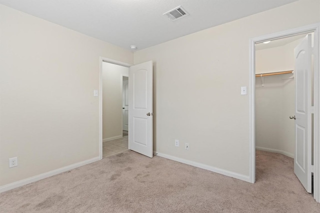 unfurnished bedroom with carpet, a walk in closet, a closet, visible vents, and baseboards