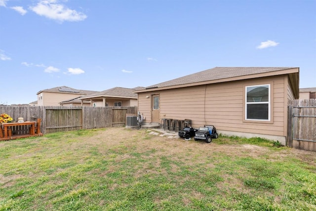 rear view of property with central air condition unit, a fenced backyard, and a lawn