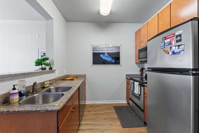 kitchen with stainless steel appliances, dark countertops, light wood-style flooring, brown cabinetry, and a sink