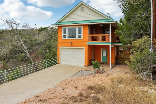 rustic home featuring concrete driveway, an attached garage, ceiling fan, fence, and metal roof