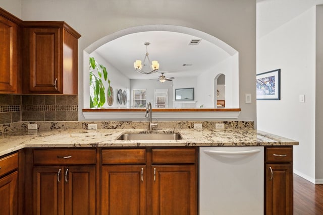 kitchen featuring visible vents, decorative backsplash, light stone counters, white dishwasher, and a sink