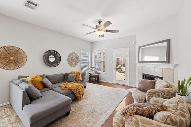 living area featuring baseboards, visible vents, a tile fireplace, ceiling fan, and wood finished floors