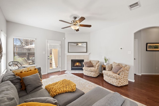 living area with arched walkways, wood finished floors, visible vents, and a tile fireplace