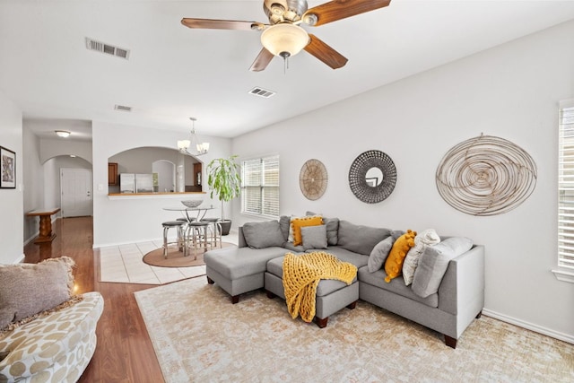 living area with ceiling fan with notable chandelier, arched walkways, wood finished floors, and visible vents