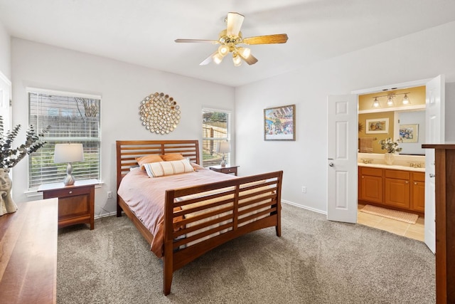 bedroom featuring connected bathroom, light colored carpet, a sink, a ceiling fan, and baseboards