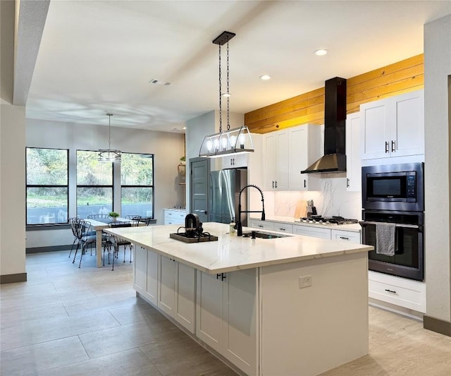 kitchen with appliances with stainless steel finishes, white cabinets, a sink, an island with sink, and wall chimney exhaust hood