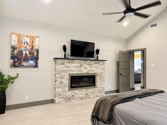 bedroom with a stone fireplace, wood finished floors, visible vents, baseboards, and vaulted ceiling