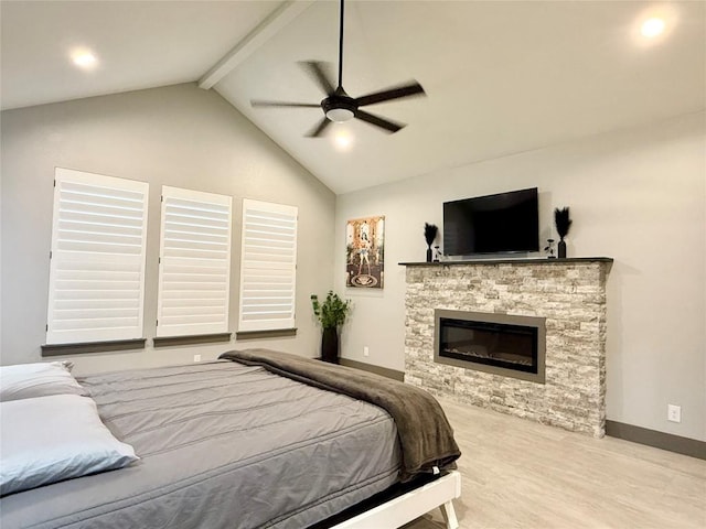 bedroom with lofted ceiling with beams, ceiling fan, a stone fireplace, wood finished floors, and baseboards