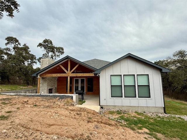 view of front facade with a chimney, board and batten siding, and french doors