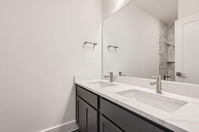 bathroom featuring double vanity, baseboards, a tile shower, and a sink