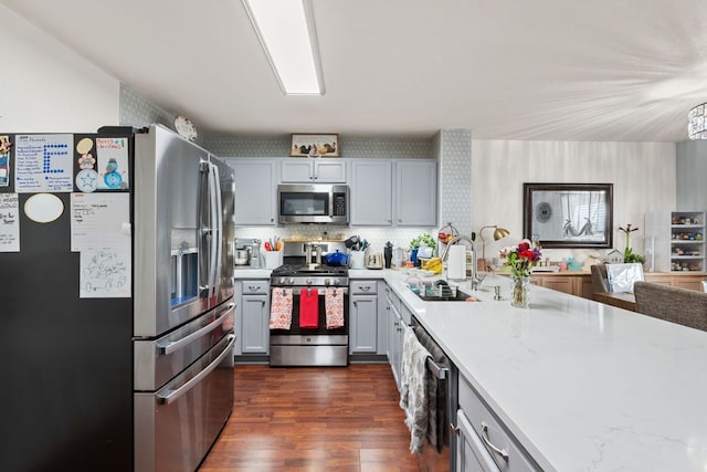 kitchen with gray cabinetry, dark wood-type flooring, a sink, appliances with stainless steel finishes, and decorative backsplash