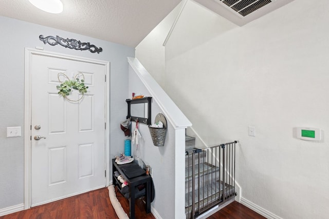 foyer featuring a textured ceiling, wood finished floors, visible vents, baseboards, and stairway