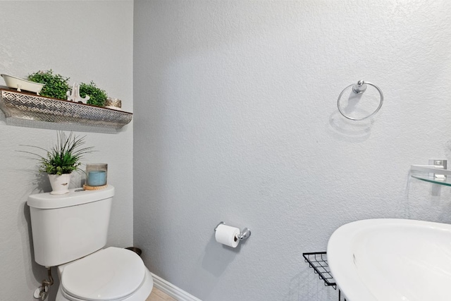 bathroom with toilet, baseboards, a sink, and a textured wall